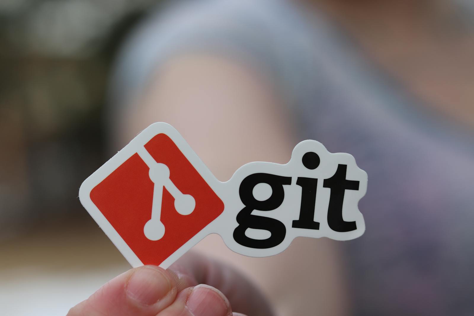 A person holding a Git sticker as part of a developer workspace