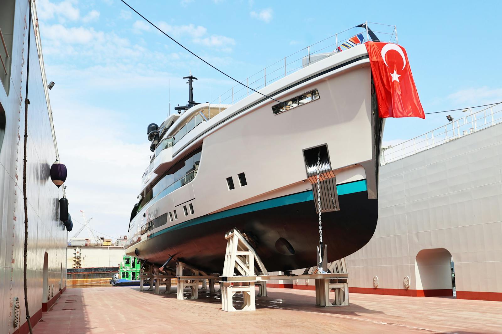 A luxury yacht moored at a shipyard with cranes in the background